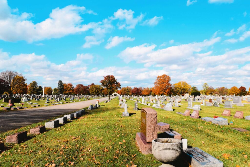 Wide view of a peaceful cemetery with neatly aligned gravestones, colorful autumn trees, and a clear blue sky, highlighting the importance of cemetery mapping software for organizing burial sites and enhancing cemetery management.